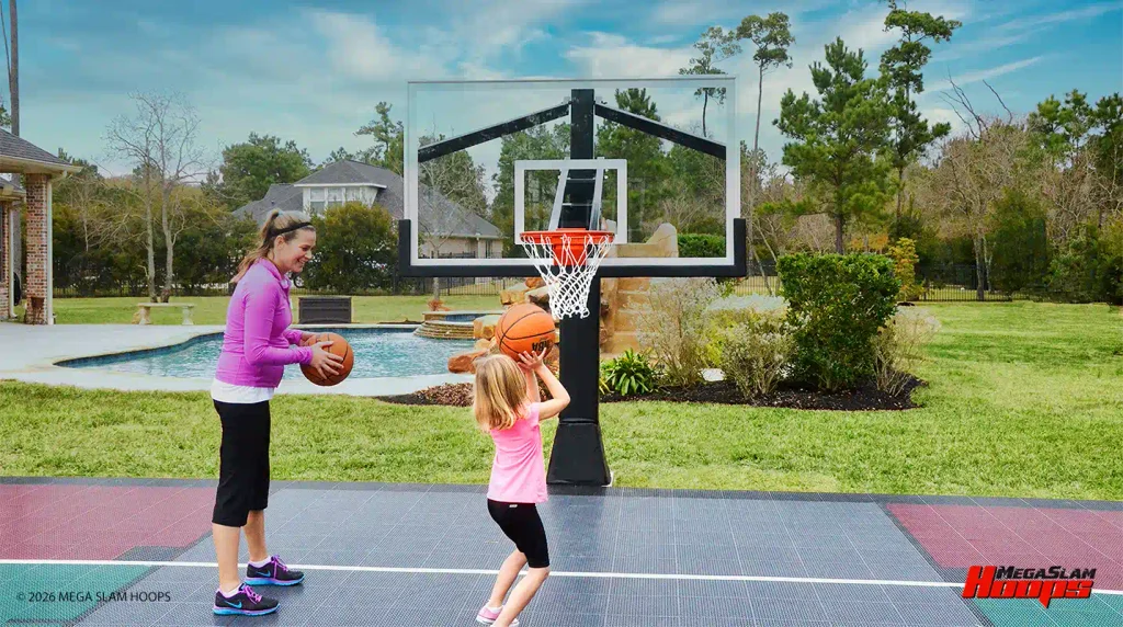 Parent teaching a child to shoot on a lowered Mega Slam adjustable hoop on a backyard court
